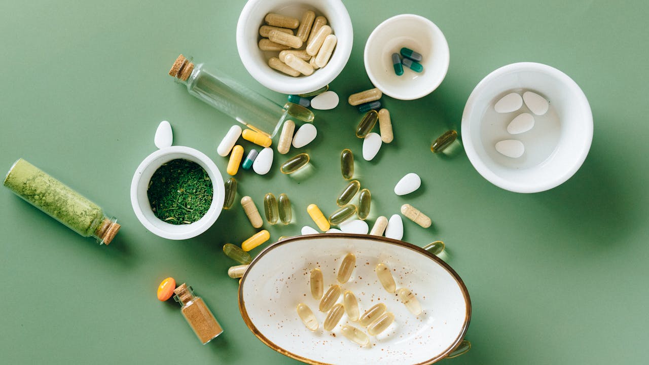 Herbal supplement capsules and botanicals arranged as a flat lay on a neutral surface