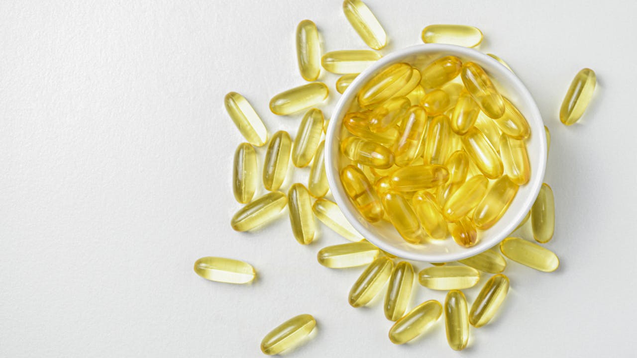 Gold fish oil supplement capsules in a flat lay arrangement with warm lighting