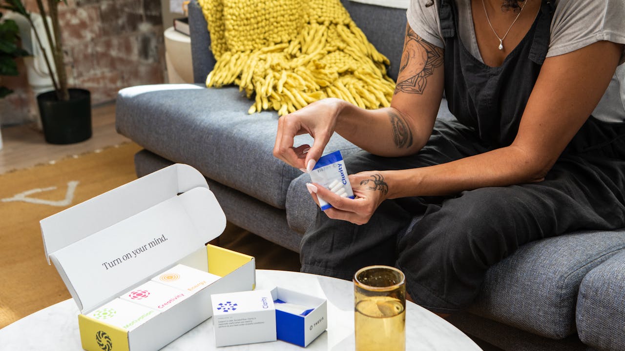 Woman at home holding supplement capsules and a glass of water