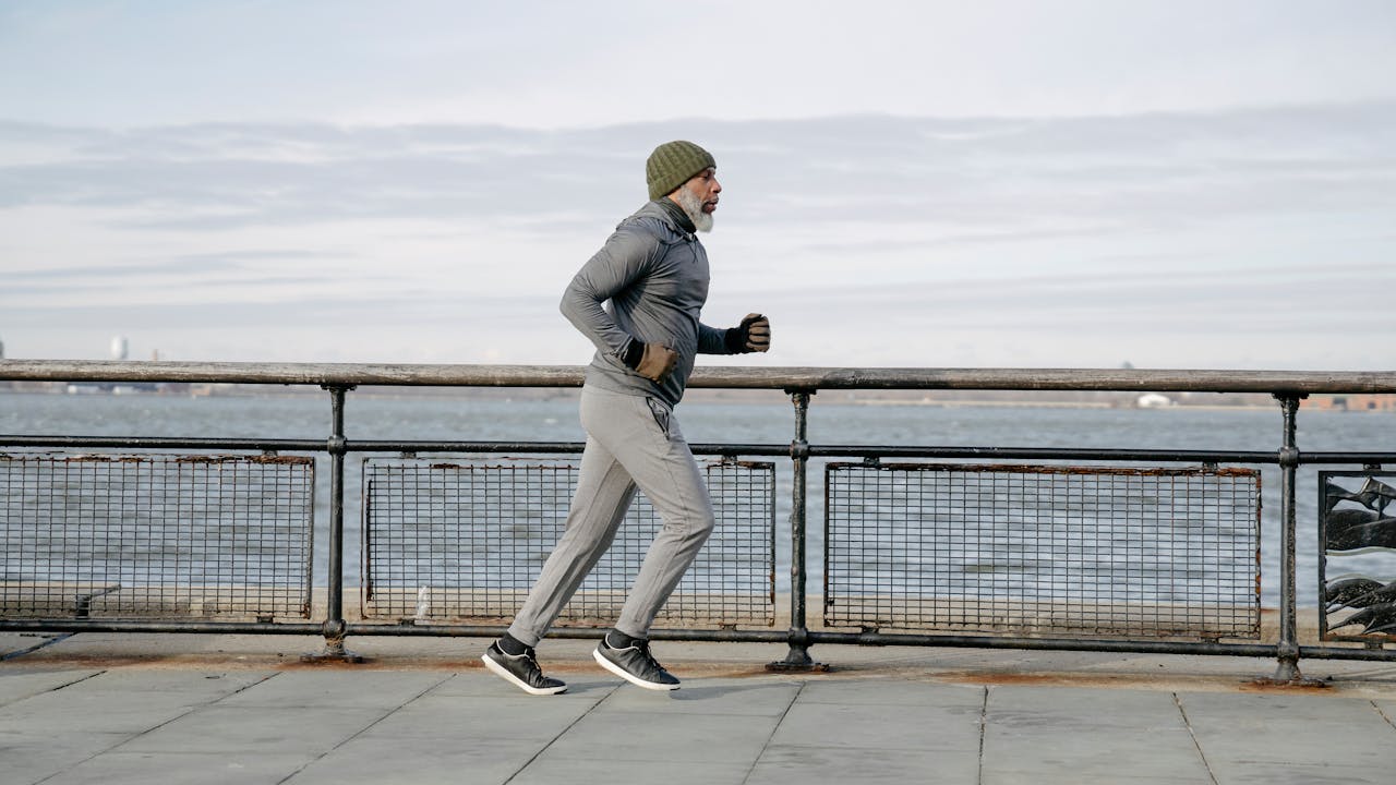 Healthy older man exercising outdoors, running in morning light, representing active longevity