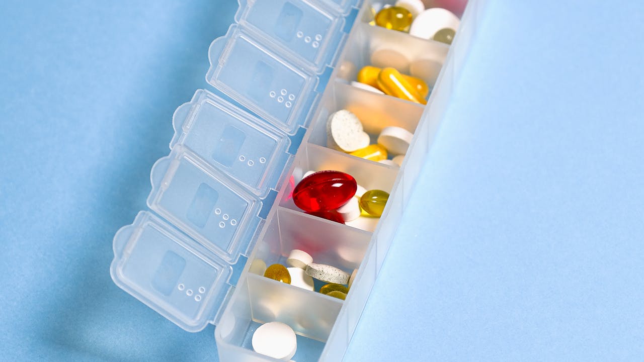 Longevity supplement capsules and pills on clean white marble surface with glass of water, representing men's longevity stack